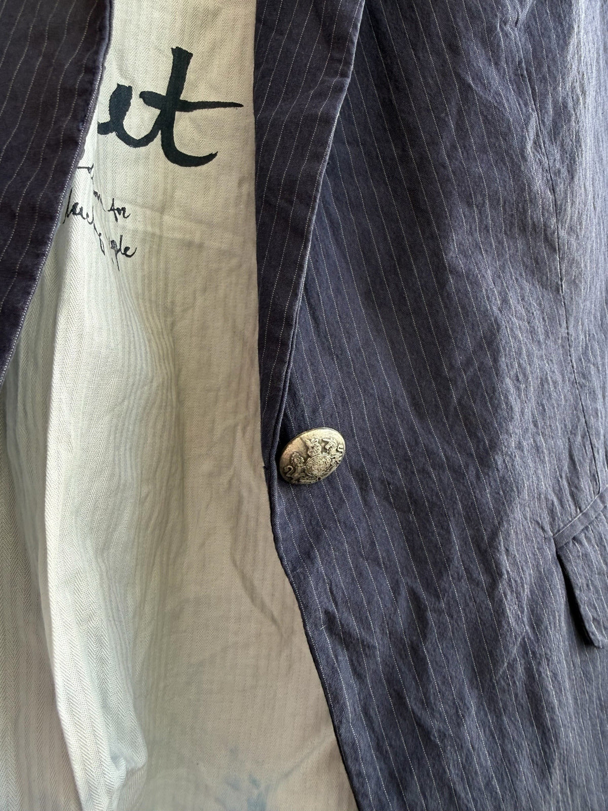 ReTrend navy pinstripe blazer with a single ornate button and a light-colored lining with text.